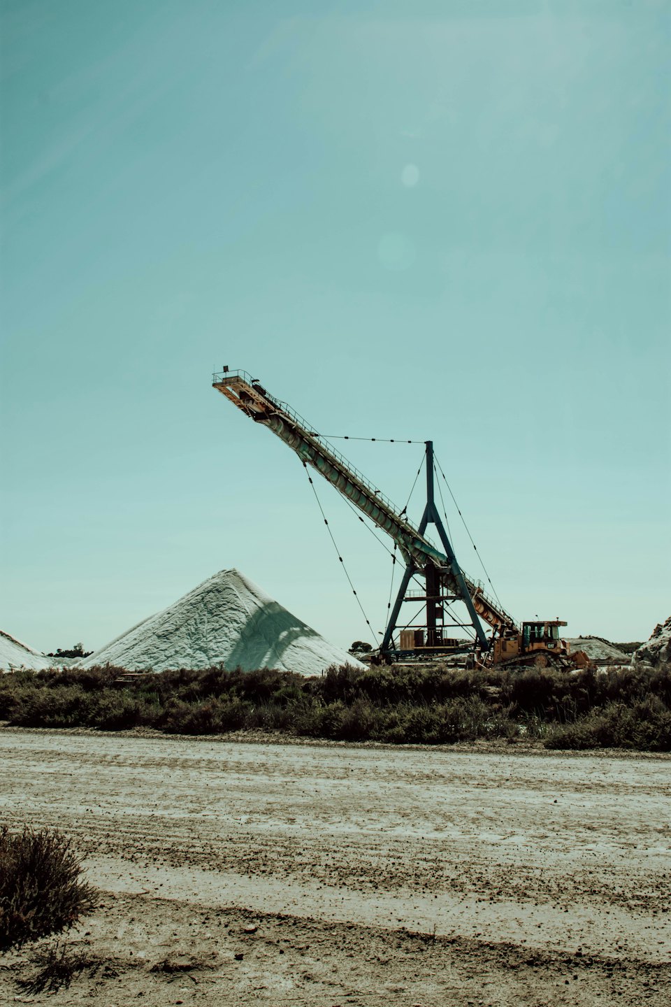 Förderband transportiert weißes Granulat durch eine trockene Landschaft.